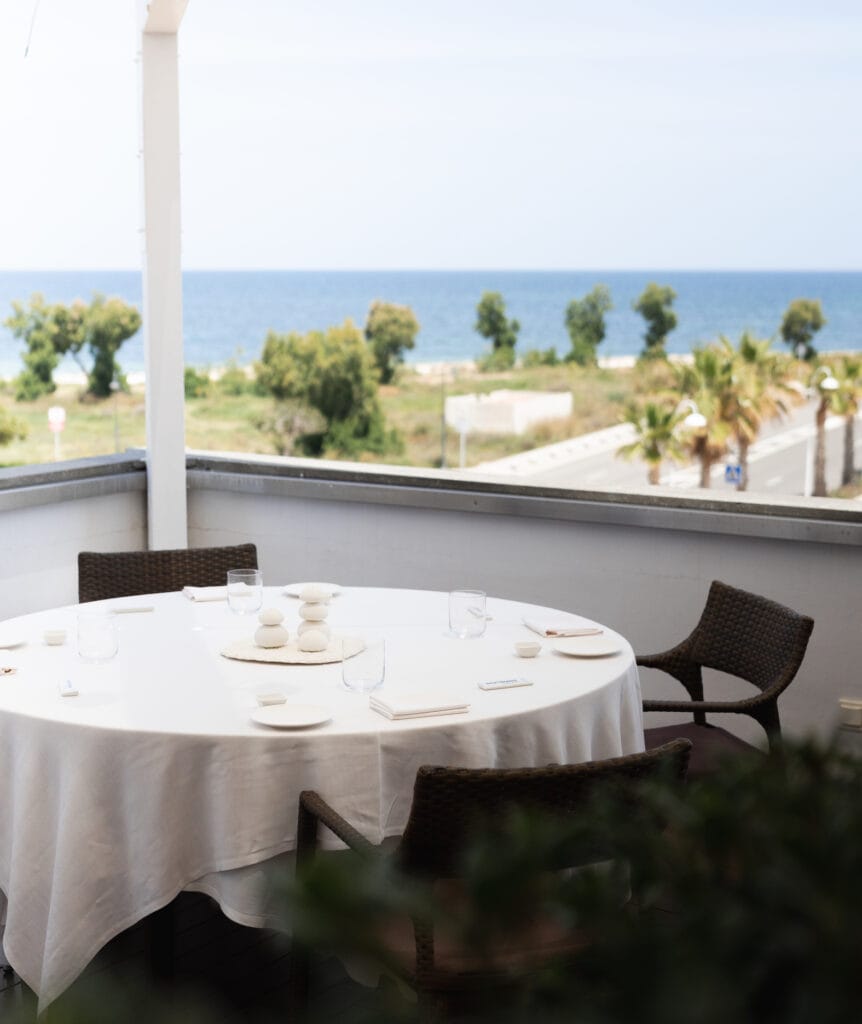 Mesa redonda elegantemente preparada en la terraza de Peix & Brases con vistas panorámicas al mar y la costa de Dénia.