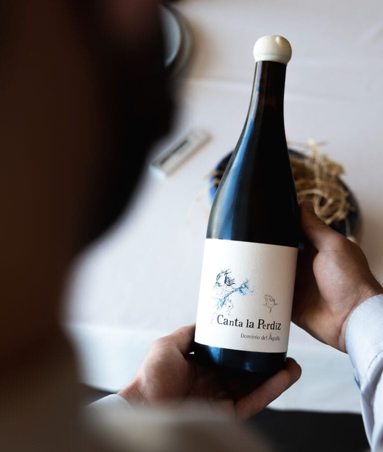 Sumiller sosteniendo una botella de vino tinto Canta la Perdiz (Dominio del Águila) en el restaurante Peix & Brases, alta gastronomía en Dénia.